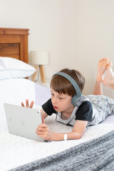 Boy wearing headphones while using his AAC iPad in bed.