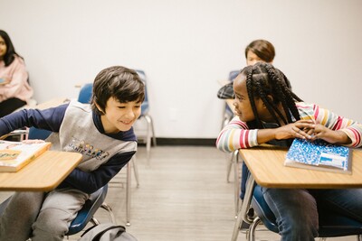     Two students communicating with each other at their desks in a classroom.